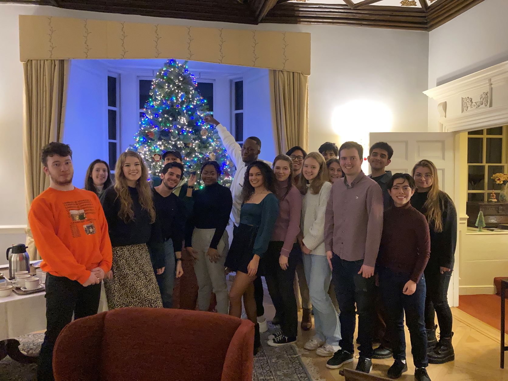 students stand smiling around the Master's Christmas tree in the Lodge